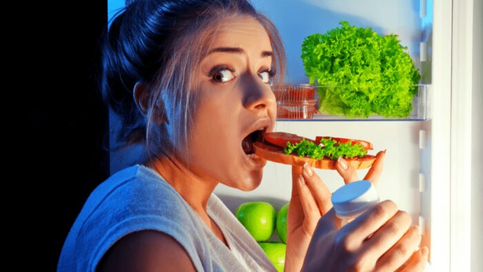 woman at refrigerator eating a sandwich late at night