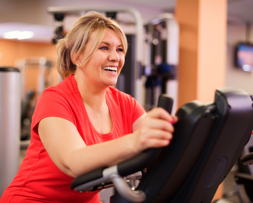 A woman wearing athletic attire pedaling on a recumbent exercise bike in a well-lit gym environment, demonstrating a focused and determined attitude towards her fitness regimen.