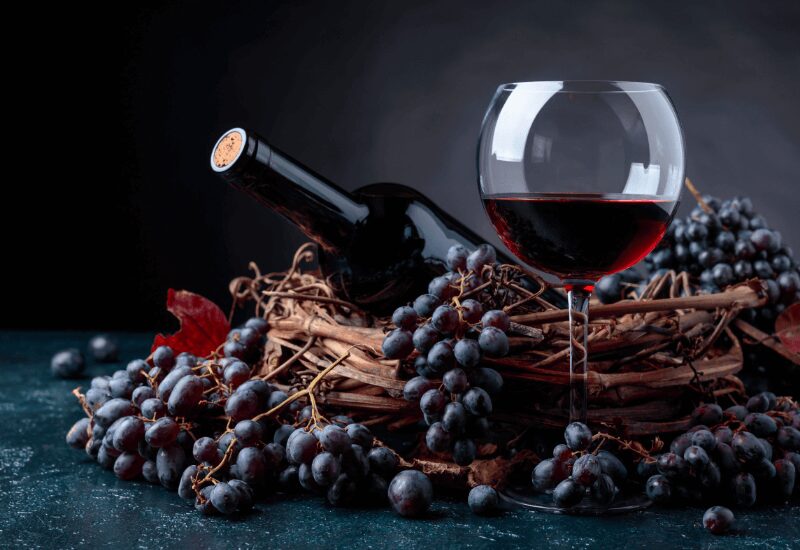 Glass of red wine with grapes and wine bottle on table