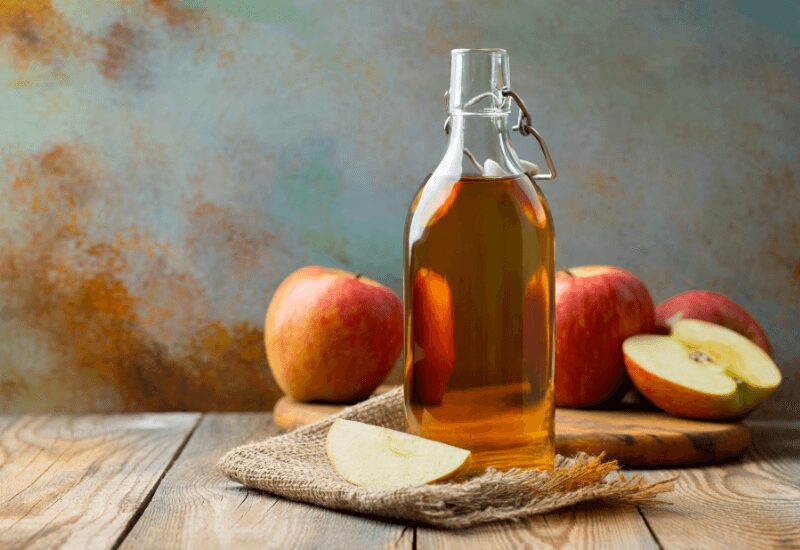 apple cider vinegar in a bottle, on table with apples