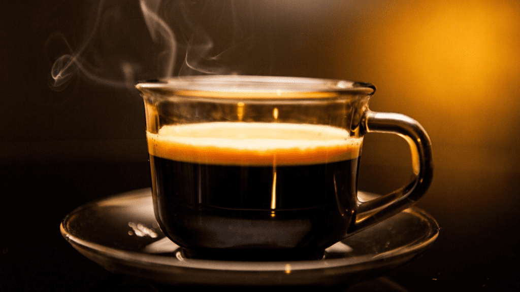 A transparent glass mug filled to the brim with freshly brewed coffee, emitting a gentle swirl of steam. The rich, dark liquid reflects a depth of flavor and warmth, promising an invigorating start to the day.