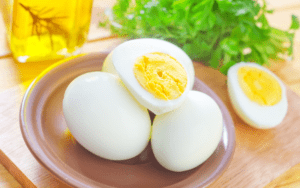 Three peeled hard boiled eggs in a row, with the middle one split open and showing its yellow yolk.