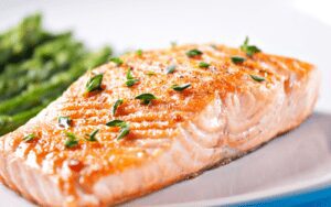 A succulent piece of baked salmon garnished with fresh herbs and served with a side of perfectly grilled asparagus spears.