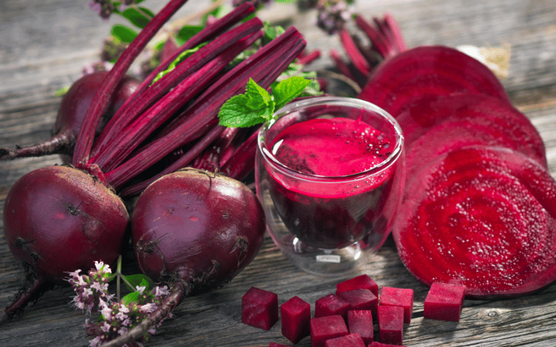 A vibrant display of beetroot in various forms: a whole beetroot with earthy tones, a clear glass filled with crimson juice, and neatly sliced beetroot pieces revealing the deep magenta hues and concentric rings inside
