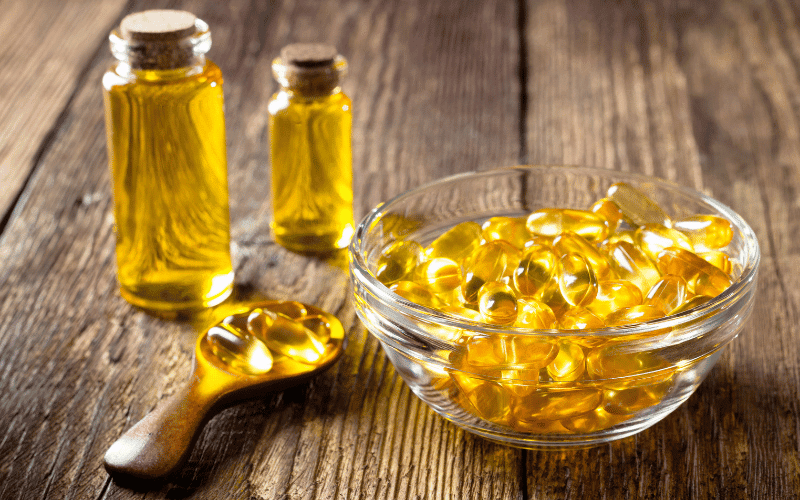 An array of golden-hued fish oil capsules is neatly spread out next to a cylindrical bottle of fish oil liquid. The translucent capsules reflect a glossy sheen, hinting at their omega-3 content