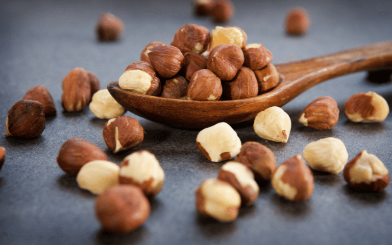 A cluster of raw hazelnuts resting on a wooden surface, their smooth, glossy shells reflecting the natural daylight