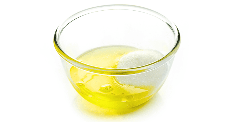 A glass bowl containing whipped egg whites, showcasing the glossy, cloud-like texture of the frothy mixture, set against a pristine white background.