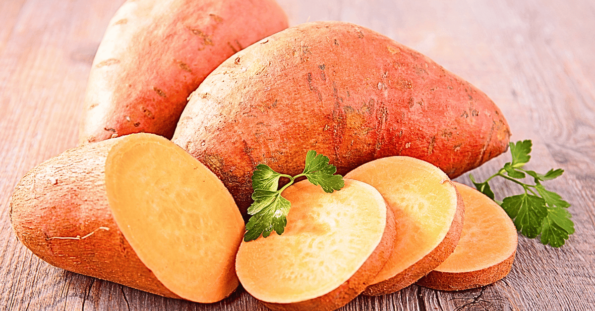 Two whole sweet potatoes, accompanied by one split open and sliced to reveal its luscious interior, elegantly garnished with fresh parsley, all presented on a rustic wooden table. 
