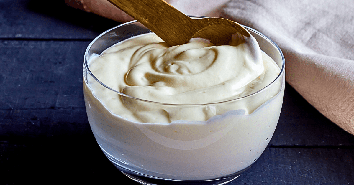 A glass bowl filled with creamy Greek yogurt, accompanied by a wooden spoon, elegantly presented on a modern wooden table.