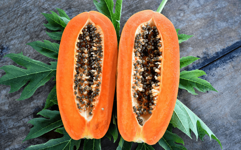 A ripe papaya split open, revealing its vibrant orange flesh and glistening black seeds, set on a rustic wooden table. The rich colors and textures capture the essence of the tropical fruit, evoking a sense of freshness and natural abundance.